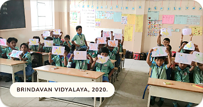 Young students holding up their drawings in a classroom at Brindavan Vidyalaya, 2020